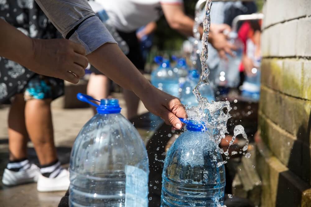 people filling large water bottles
