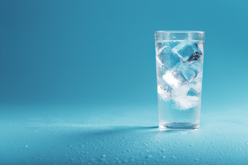 A glass of ice cold water against an aqua background