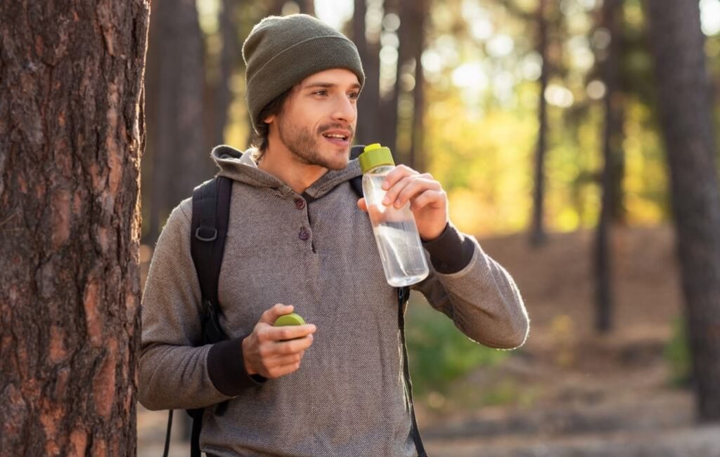 Man drinking water from a reusable water bottle in the forest