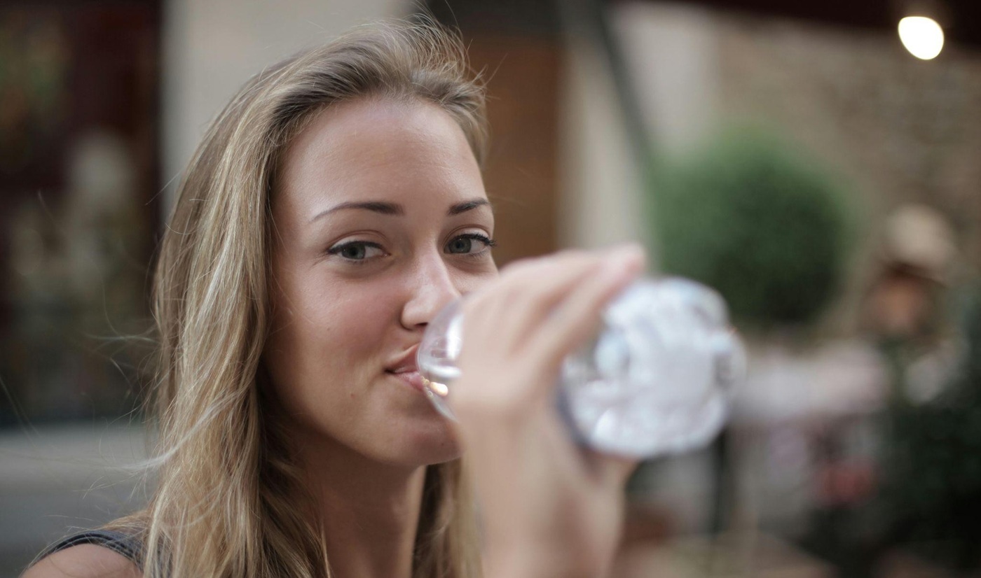 Woman drinking water out of a bottle while smiling at the camera