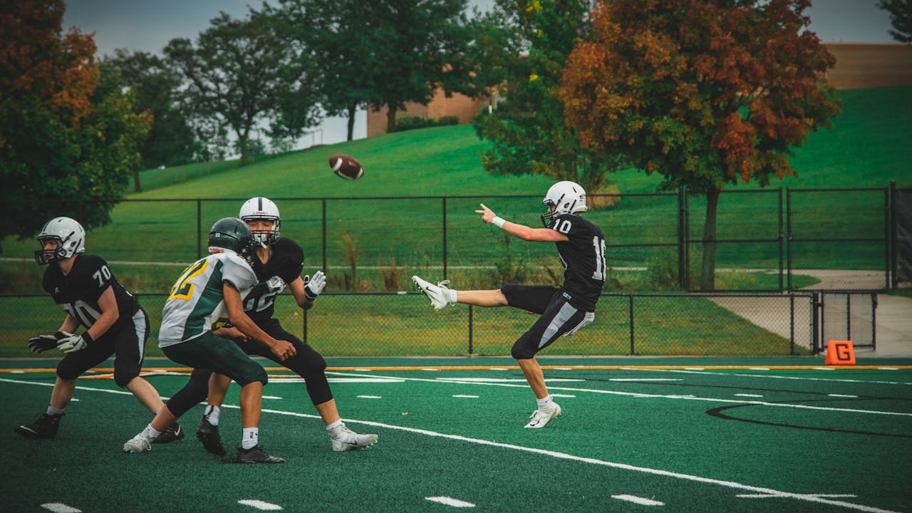 player kicking a football while two other players block an opponent