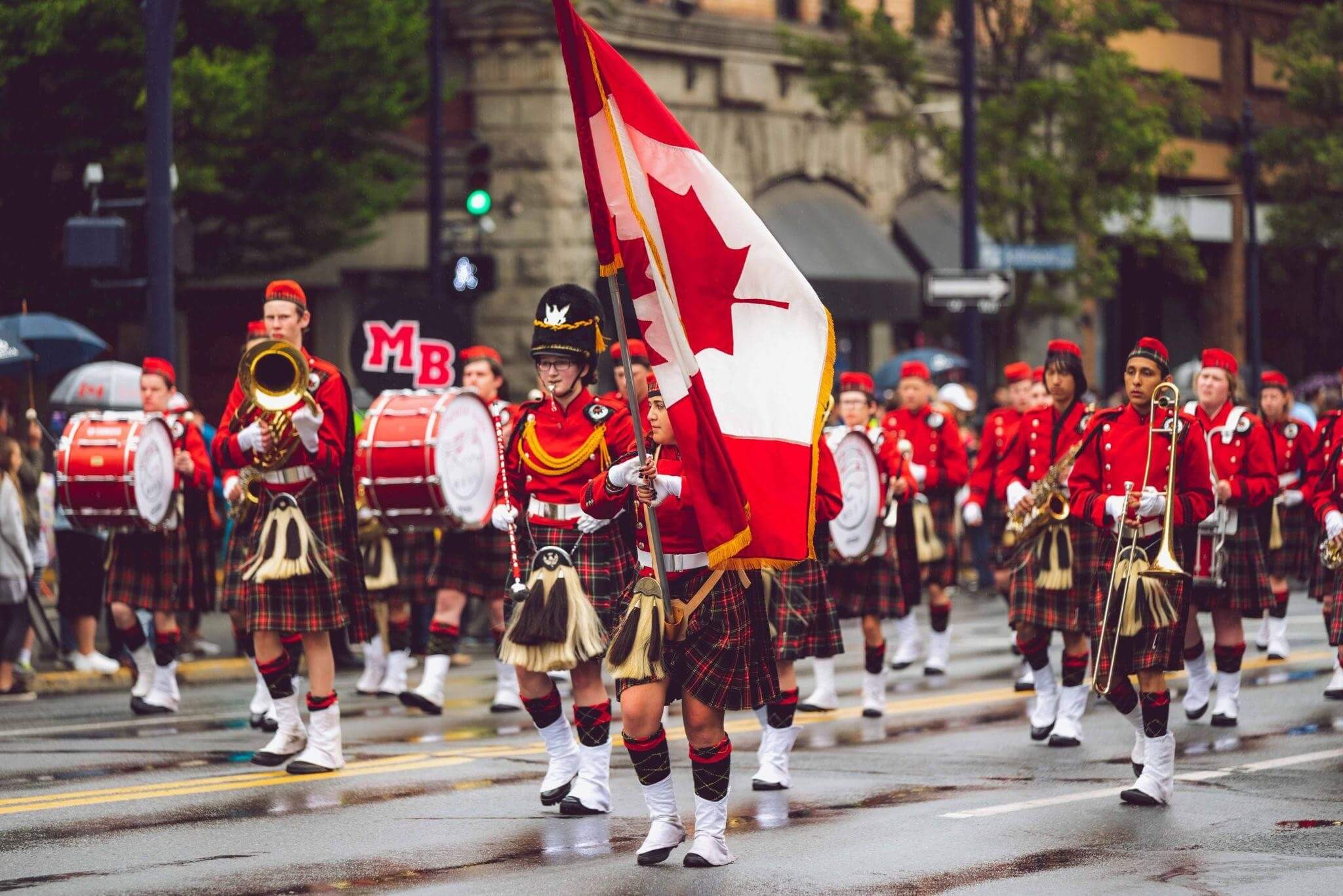 Marching band dressed in uniform and marching in a parade with a Canadian flag